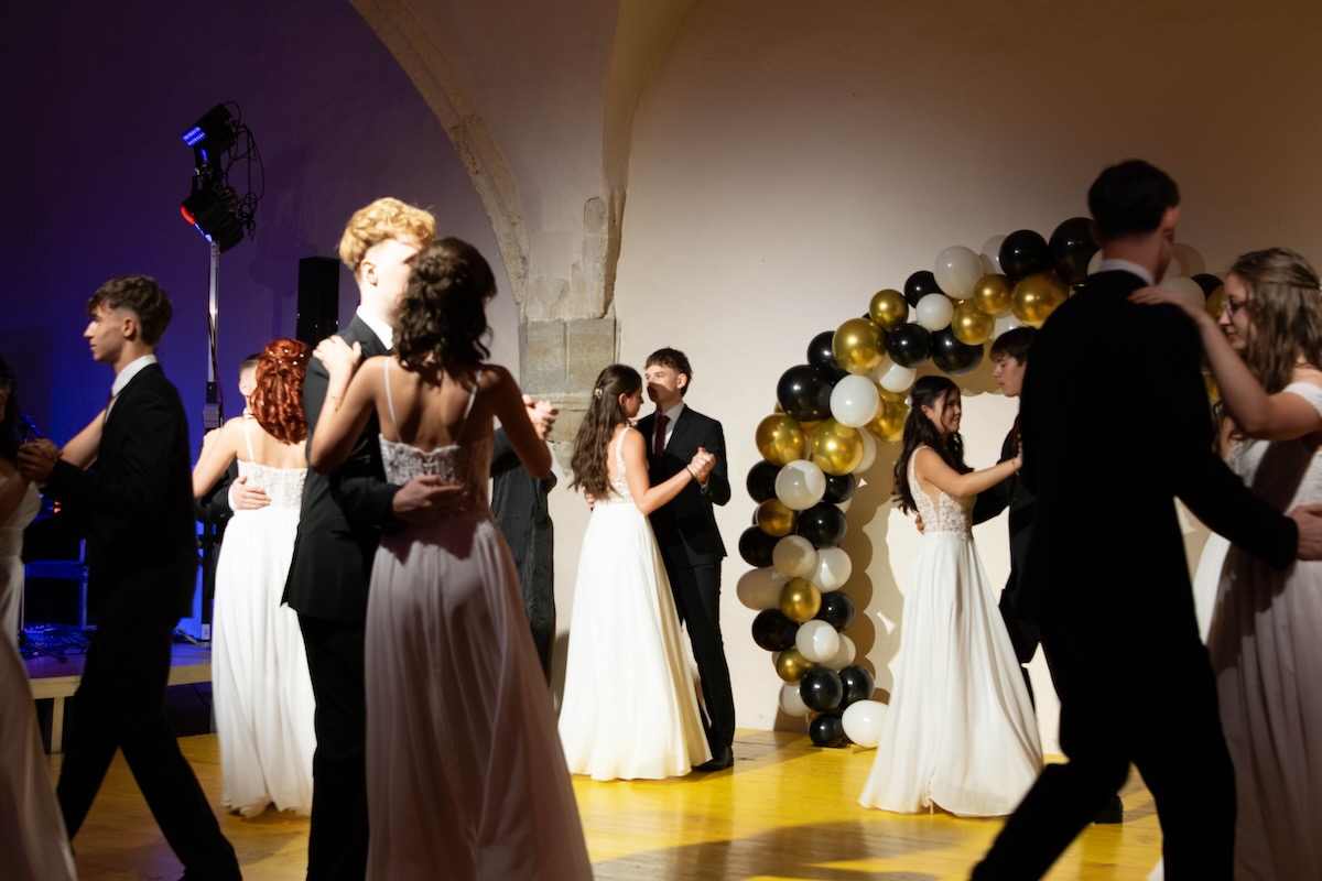 Ballgäste tanzen im Festsaal vor einer Ballondekoration in Schwarz, Gold und Weiß
